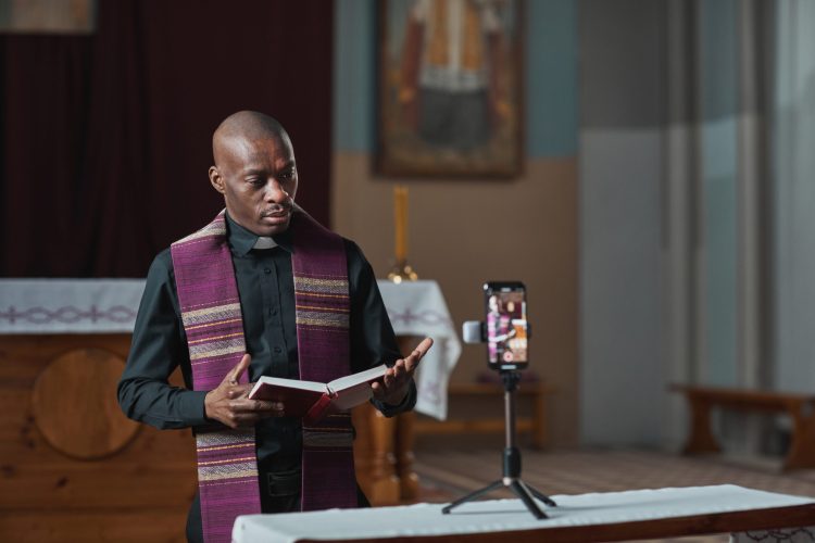 African priest holding Bible and performing during live broadcast on mobile phone online